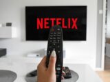 pessoa segurando controle remoto da TV e ligando na Netflix